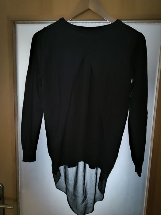 Camisola preta pedras de brilho e abertura com transparência atrás.