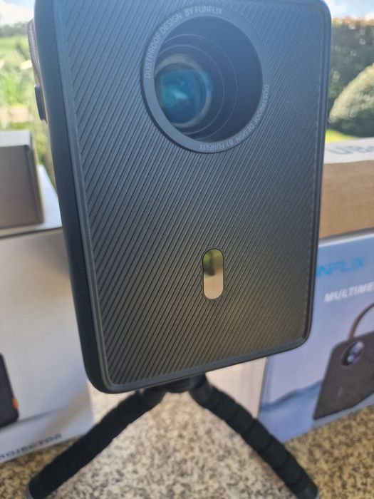 projetor portátil FunFlix G1 com alça de transporte.O dispositivo possui conectividade Wi-Fi 5G oferta de tripé