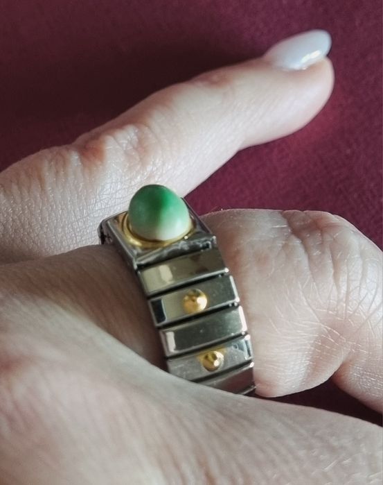 Anel prateado, em aço, com apontamentos dourados e pedrinha verde.