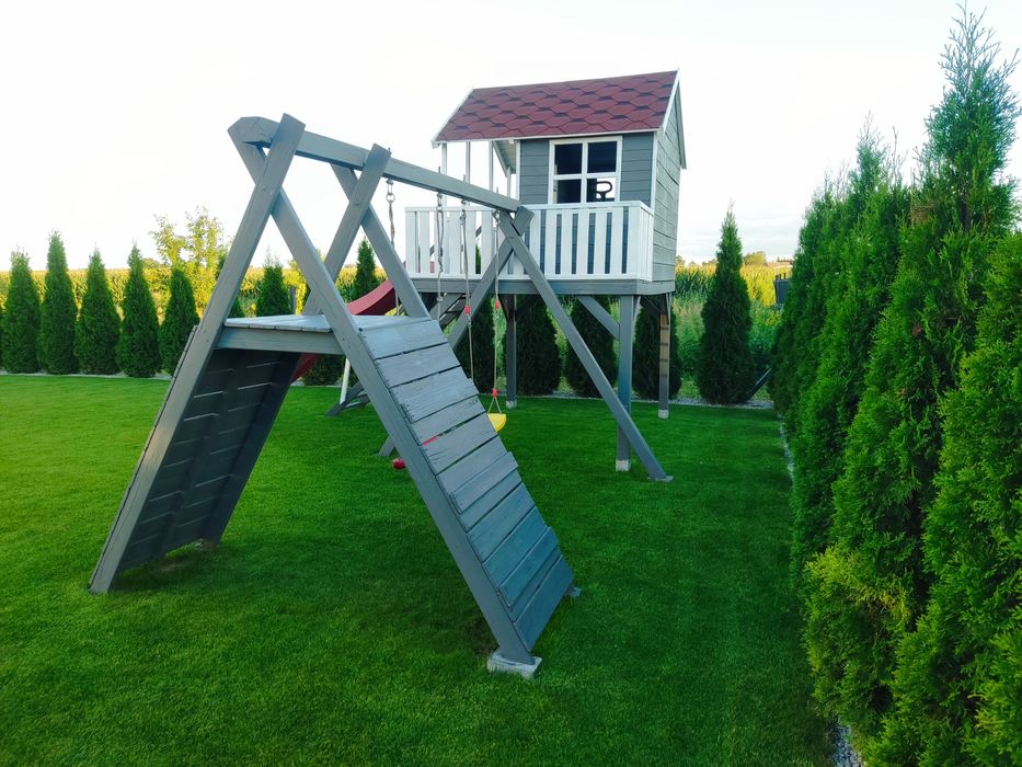 Duży drewniany domek dla dzieci ze zjeżdżalnią, huśtawkami, wspinaczką