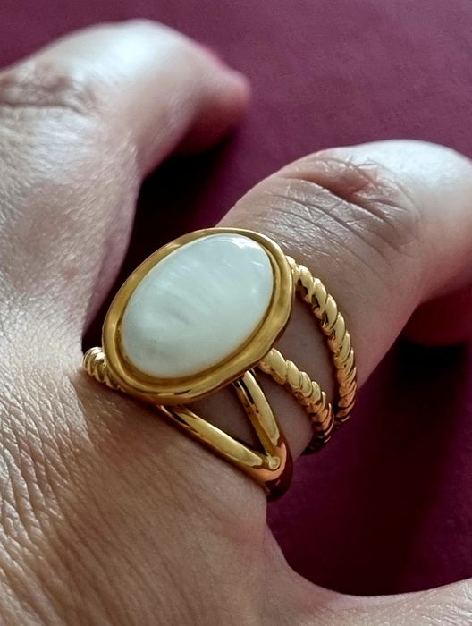 Anel dourado, em aço, com uma  madrepérola  oval no centro. Ajustável