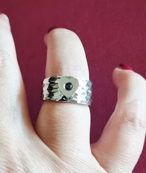 Anel prateado, em aço, com 1 coração com pedrinha preta no centro. T17