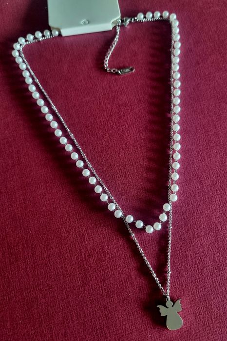 Colar duplo, em aço, 1 de pérolas e 1 com anjinho. Tem extensor