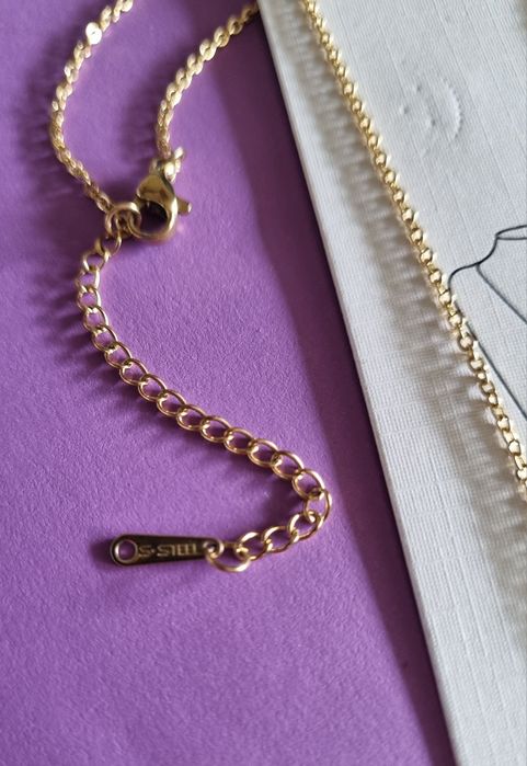 Colar dourado, em aço, com 2 trevos pendentes. Formato gravata.