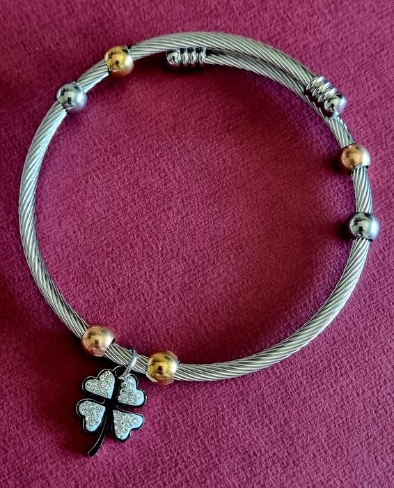 Pulseira prateada, em aço, com bolinhas douradas e um trevo da sorte.