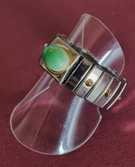 Anel prateado, em aço, com apontamentos dourados e pedrinha verde.