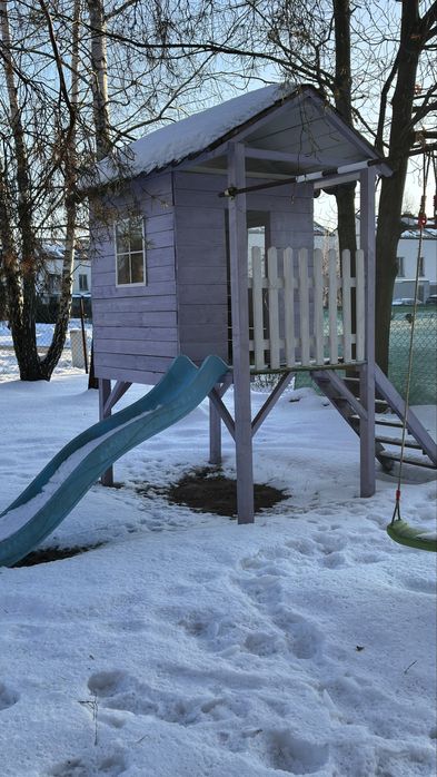 Drewniany domek dla dzieci na podwyższeniu ze zjeżdżalnią i huśtawką