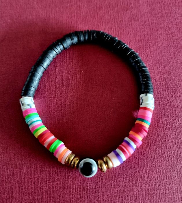 Pulseira elástica em tons de preto e multicor. Com olho de proteção