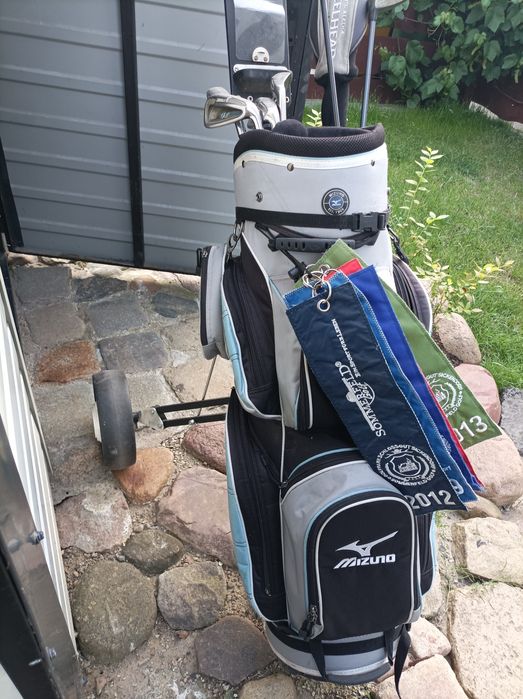 Zestaw kijów golfowych wraz z torbą i wózkiem.