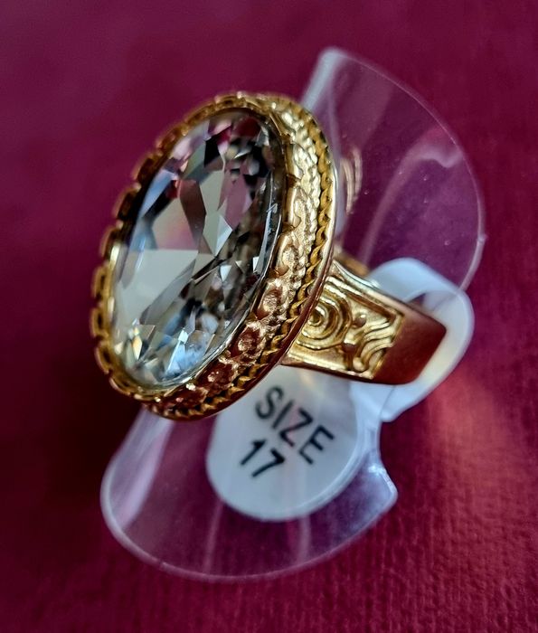 Anel dourado, em aço, com grande pedra de vidro transparente oval. T17