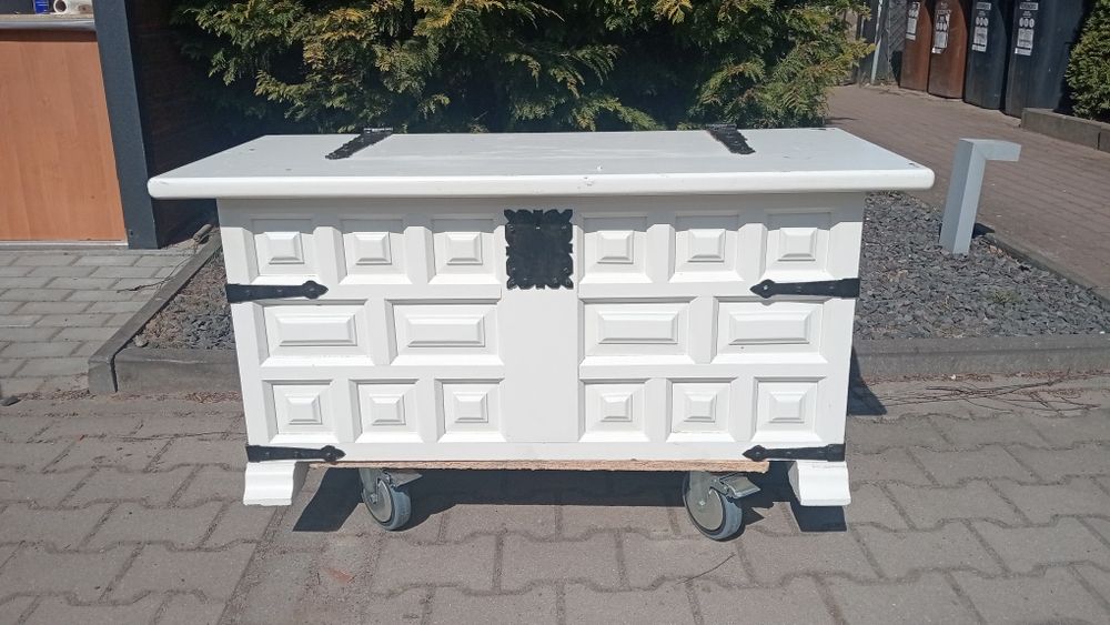 Biała duża skrzynia, kufer z czarnymi okuciami.