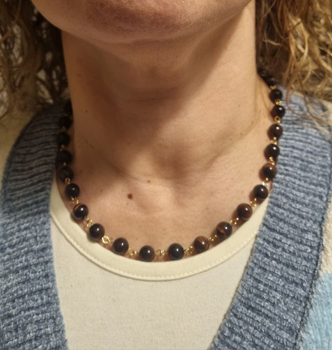 Colar dourado, em aço, às bolinhas castanhas de pedra natural "olho de gato". Tem extensor.