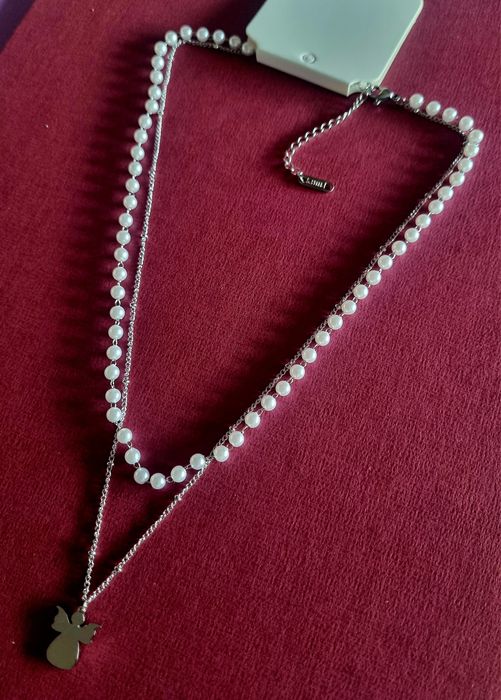 Colar duplo, em aço, 1 de pérolas e 1 com anjinho. Tem extensor