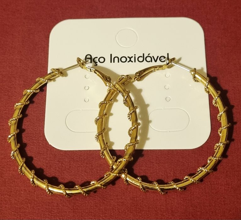Brincos/argolas douradas, em aço, com cerca de 5cm de comprimento.