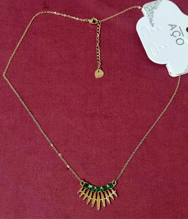 Colar dourado, em aço, com 5 pedrinhas quadradas verdes. Tem extensor.