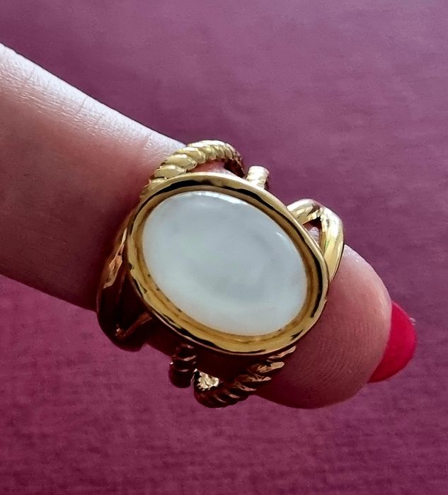 Anel dourado, em aço, com uma  madrepérola  oval no centro. Ajustável