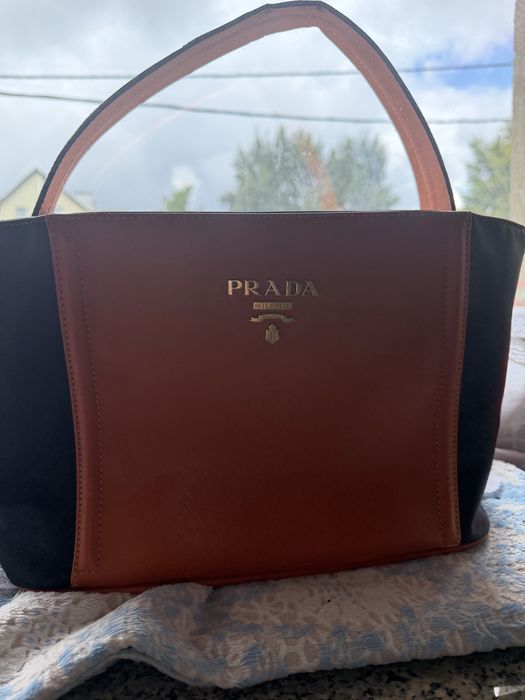 Pomarańczowo-czarna skórzana torebka Prada Saffiano z wyraźnym metalowym logo z przodu.