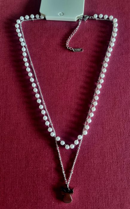 Colar duplo, em aço, 1 de pérolas e 1 com anjinho. Tem extensor