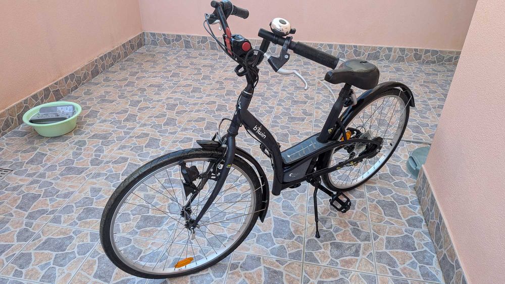 bicicleta  B'Twin Elops, apresentando um quadro de design urbano em preto.Modelo: B'Twin Elops 3 ou Elops 300. Inclui guarda-lamas e um selim preto.