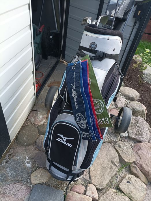 Zestaw kijów golfowych wraz z torbą i wózkiem.