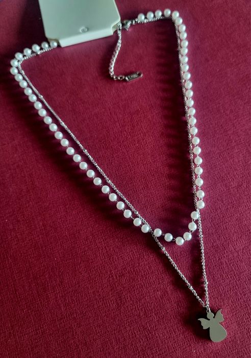 Colar duplo, em aço, 1 de pérolas e 1 com anjinho. Tem extensor