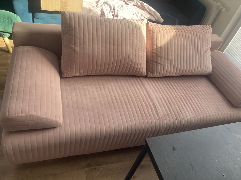 Rozkładana kanapa w ładnym, jasnoróżowym kolorze.