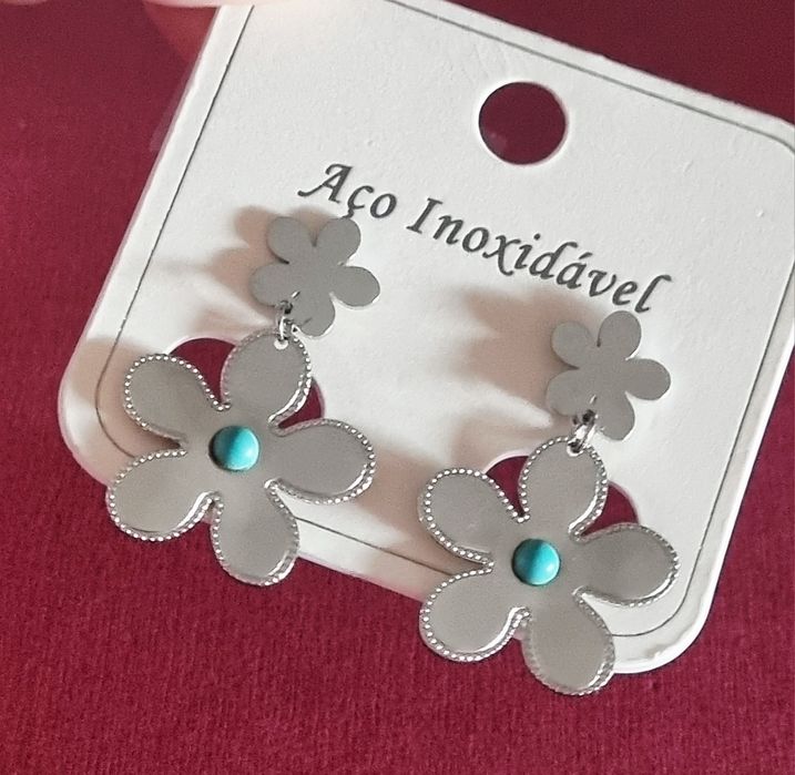 Brincos prateados, em aço, 2 flores de diferentes tamanhos com 1 pedrinha turquesa.