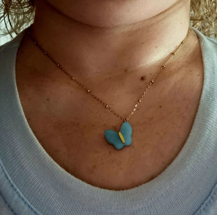 Colar dourado, em aço, malha com bolinhas e pingente borboleta azul.