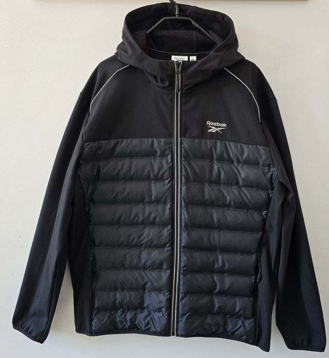 Czarna kurtka hybrydowa marki Reebok z kapturem charakteryzuje się pikowanym panelem.