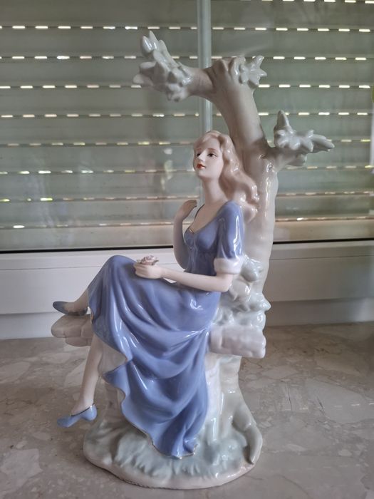 Piękna porcelanowa figurka dziewczyna siedząca na drzewie