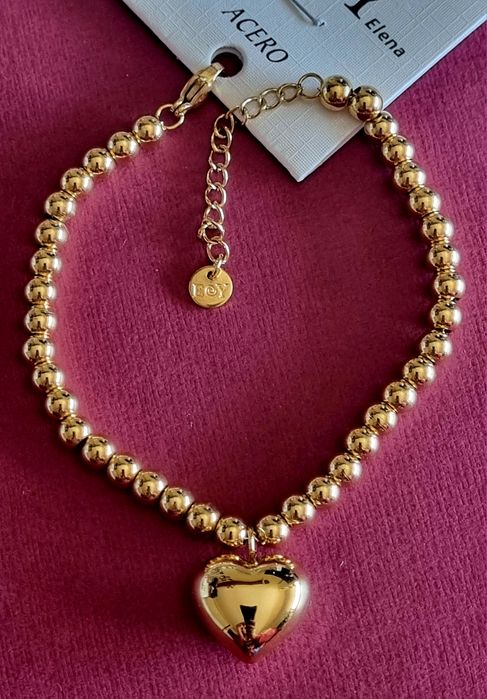 Pulseira dourada, em aço, toda às bolinhas e com 1 coração. Tem extens