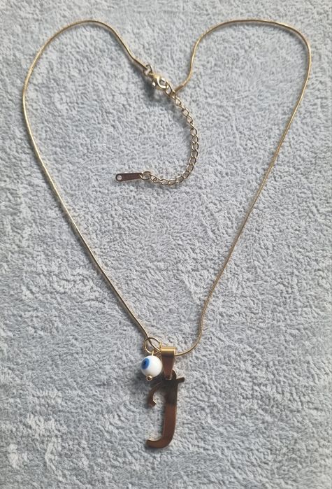 Colar dourado, em aço, com a letra "J" e olho turco. Tem extensor