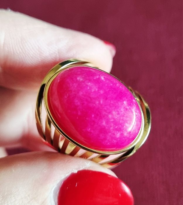 Anel dourado, em aço, com pedra oval rosa fucsia. 18/ajustável