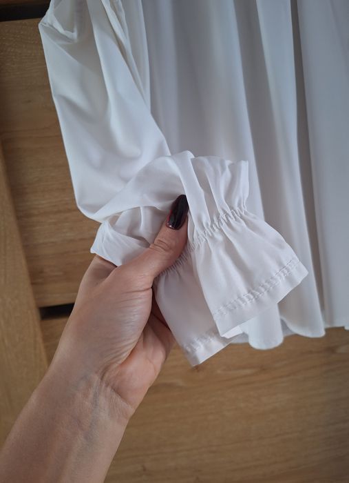 Biała bluzka z wycięciem na ramiona i ozdobnym wiązaniem na tyle