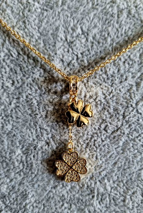 Colar dourado, em aço, com 2 trevos pendentes. Formato gravata.