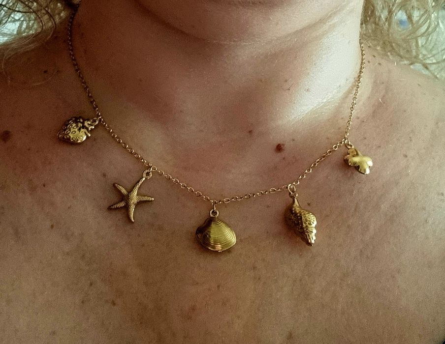 Colar dourado, em aço, com 5 pingentes diferentes. Tem extensor.