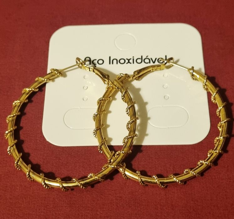 Brincos/argolas douradas, em aço, com cerca de 5cm de comprimento.