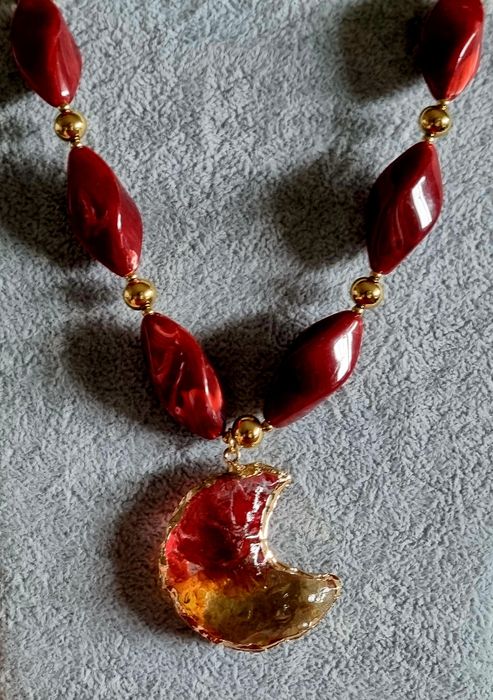 Colar dourado, em aço, com peças bordeaux em acrílico e uma meia lua.