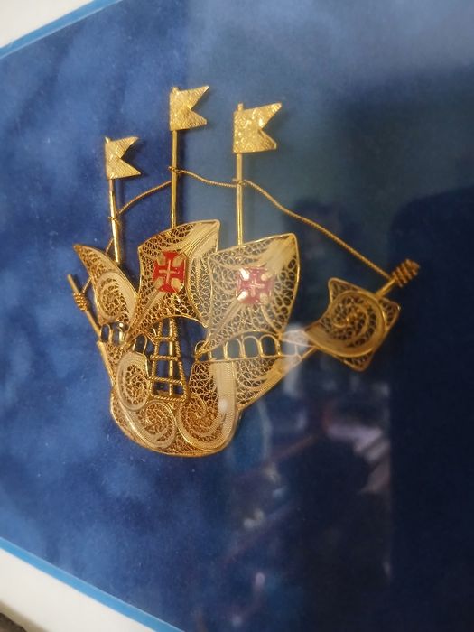 Moldura com miniatura de caravela portuguesa tradicional em filigrana de prata dourada.O navio apresenta velas detalhadas com a Cruz de Cristo .