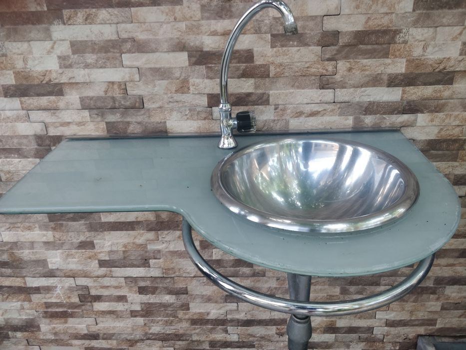 Móvel lavatório em vidro e inox com toalheiro e torneira.