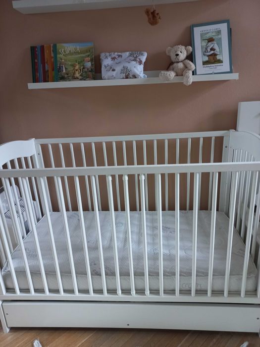 Białe łóżeczko dziecięce z materacem.