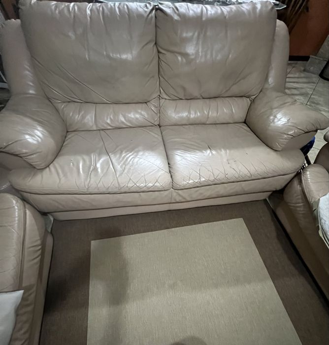 Sofá  em pele , na cor bege , com alguns desgastes  pelo uso .