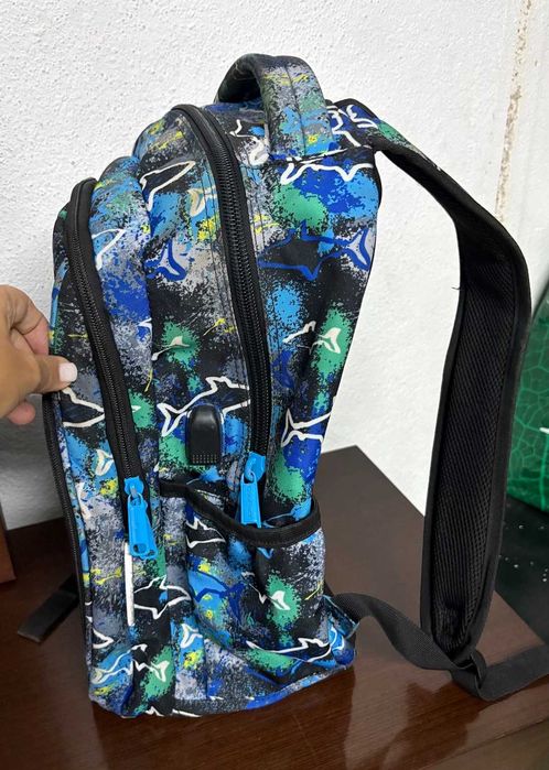 Mochila escolar CoolPack em tons azul, verde e preto, com padrão de tubarões.