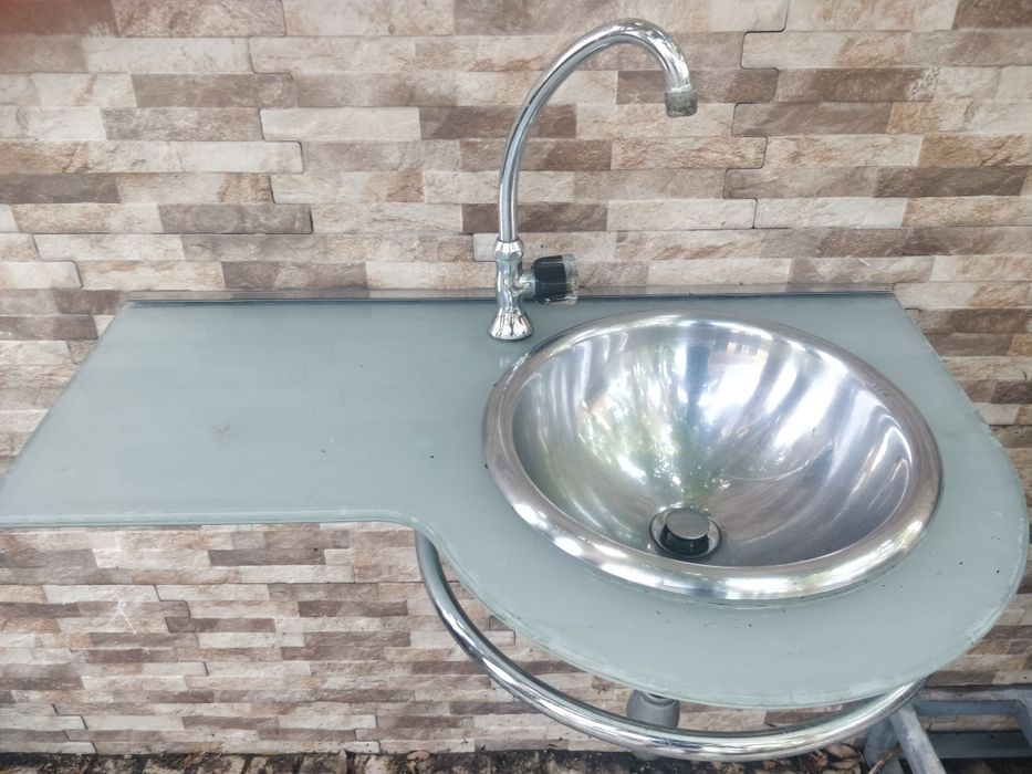 Móvel lavatório em vidro e inox com toalheiro e torneira.