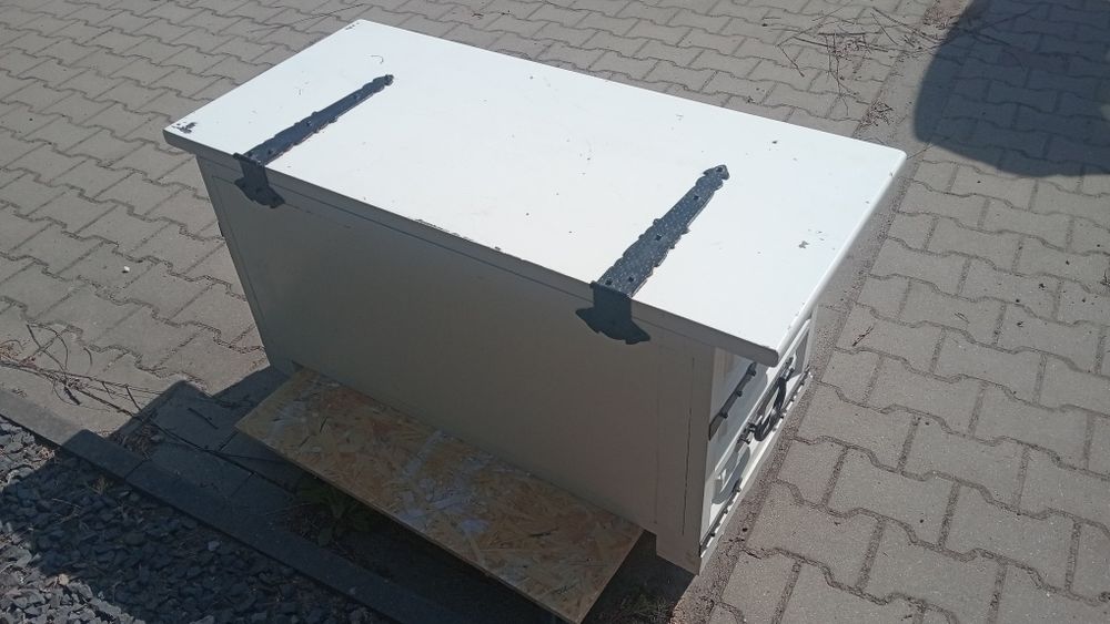 Biała duża skrzynia, kufer z czarnymi okuciami.