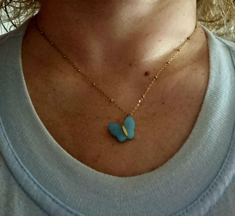 Colar dourado, em aço, malha com bolinhas e pingente borboleta azul.