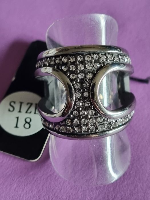 Anel prateado, em aço, aberto dos lados e cheio de zirconias. T17/18
