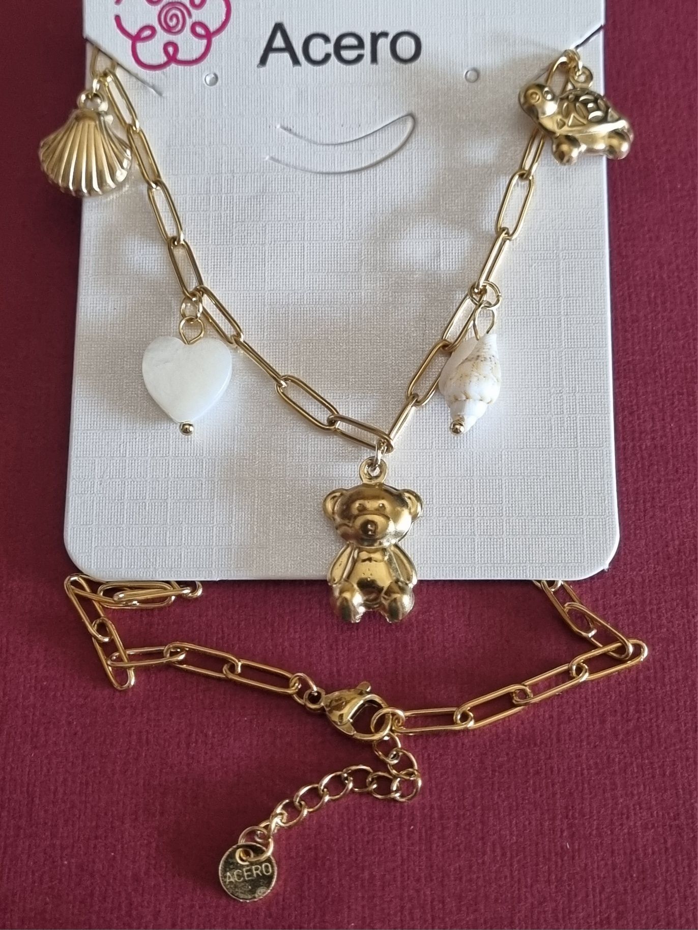 Colar dourado, em aço, com 5 pingentes diferentes. Tem extensor