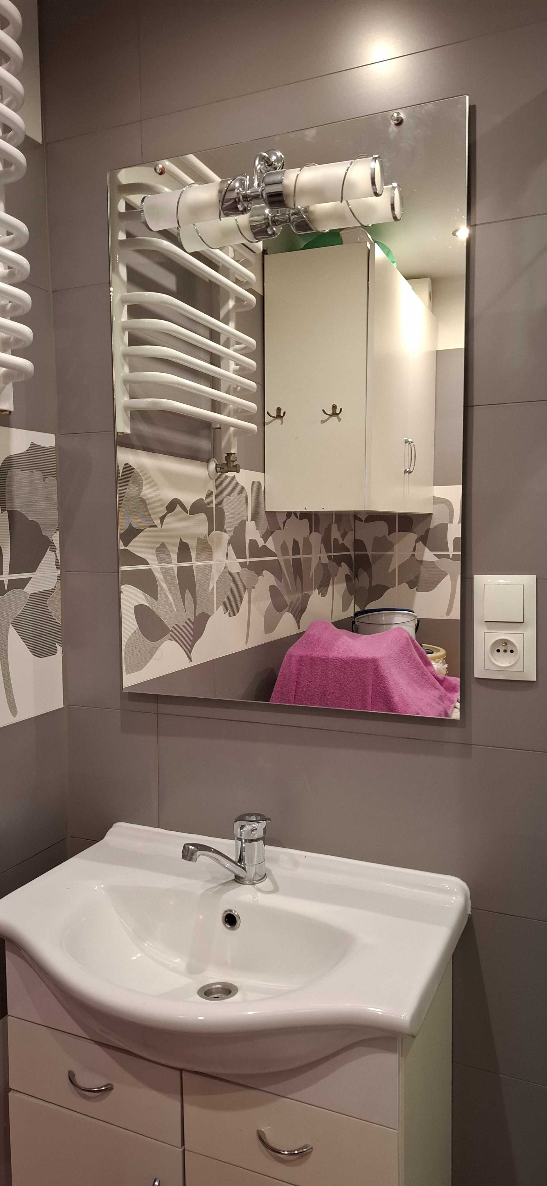 Meble łazienkowe: lustro z kinkietem, umywalka, szafka.