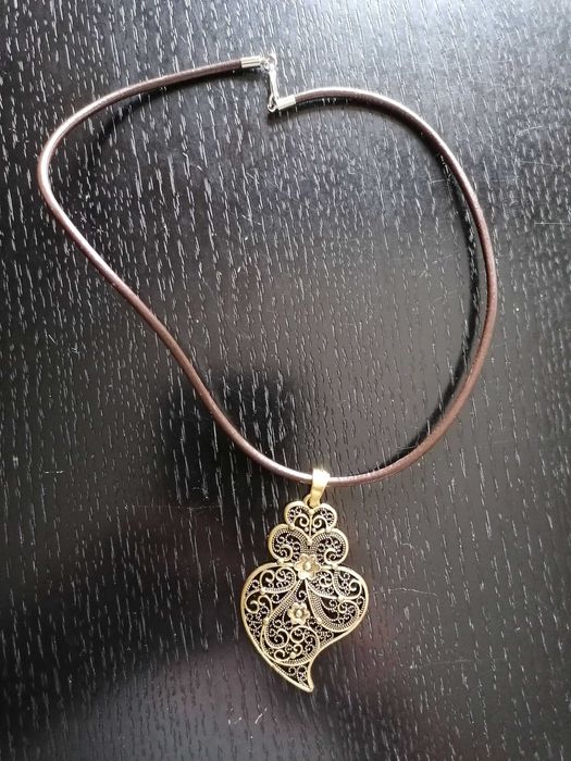 Fio em couro com pendente de coração de Viana em metal amarelo.